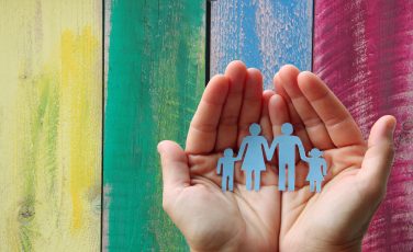 Paper family in hands on wooden coloured background welfare concept
